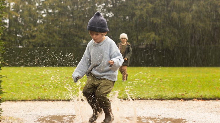 Boy jumping in a puddle. The boy is wearing a woolly hat and wellies